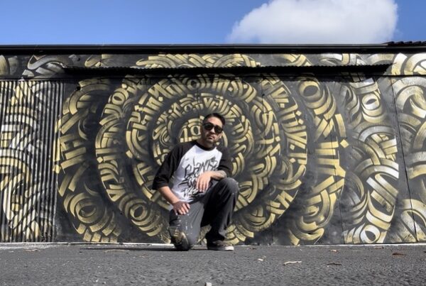 Zak Perez kneeling in front of his mural at the Blue Lot