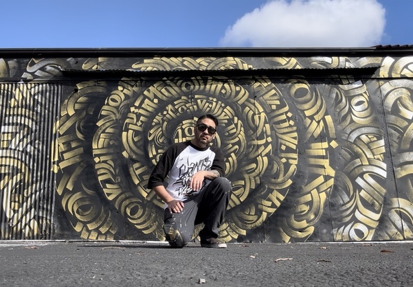 Zak Perez kneeling in front of his mural at the Blue Lot