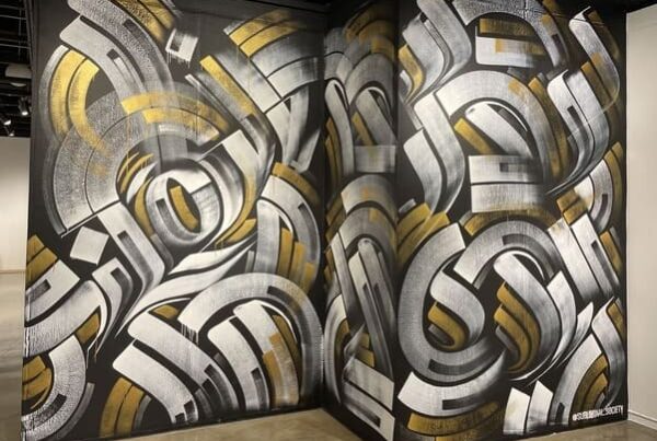 White, gold and silver calligraffiti mural on a black wall at El Camino College by Zak Perez