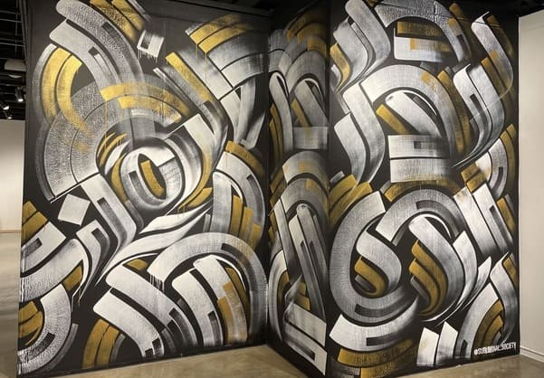 White, gold and silver calligraffiti mural on a black wall at El Camino College by Zak Perez