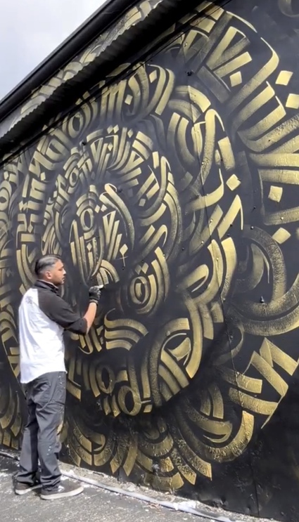 Zak Perez painting a calligraffiti, mandala mural at the Blue Lot